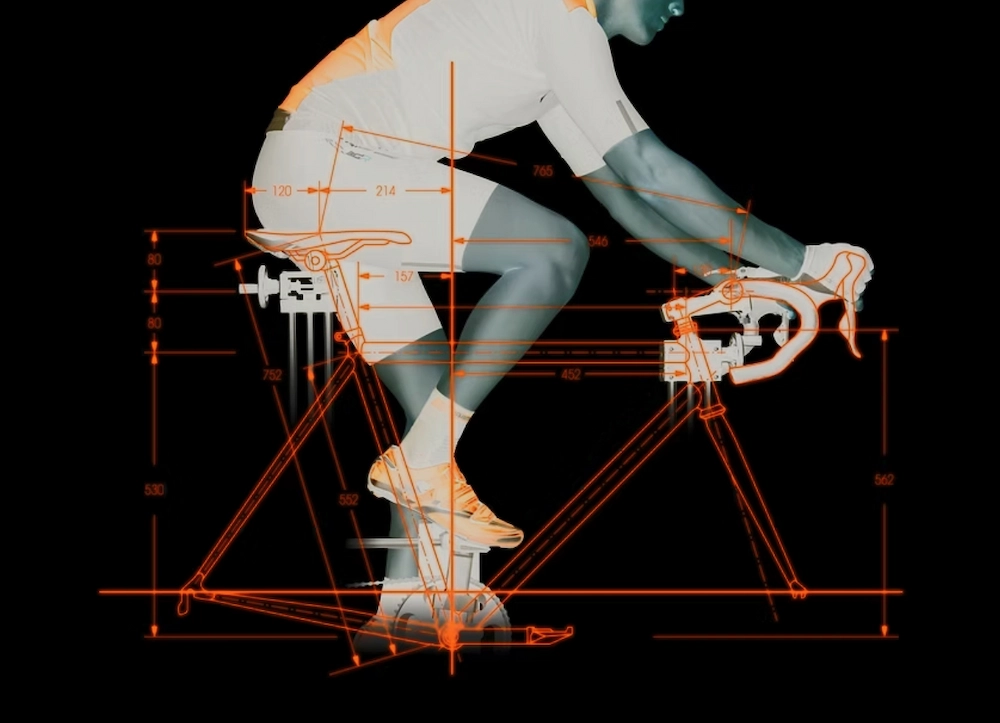 Ciclista su bici da corsa ripreso di profilo, con sovrapposizione di linee e misure arancioni che illustrano i parametri di un bike fitting professionale.